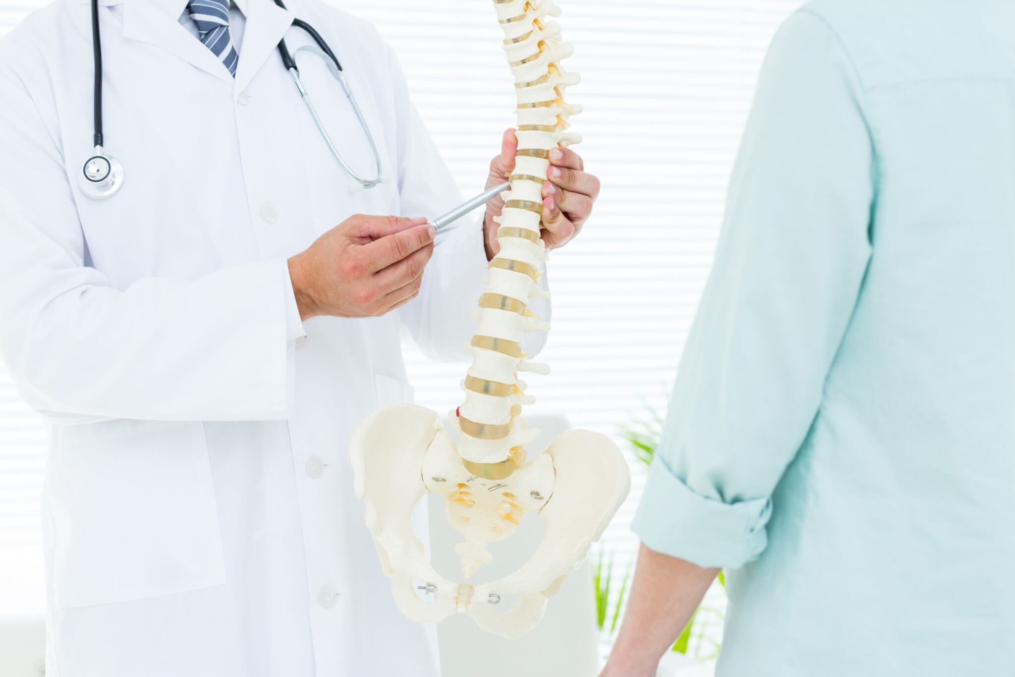 Spine specialist explaining scoliosis and surgical treatment options using an anatomical spine model.